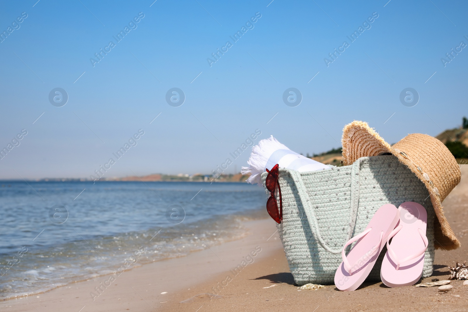 Photo of Bag with beach accessories and flip flops on seaside. Space for text