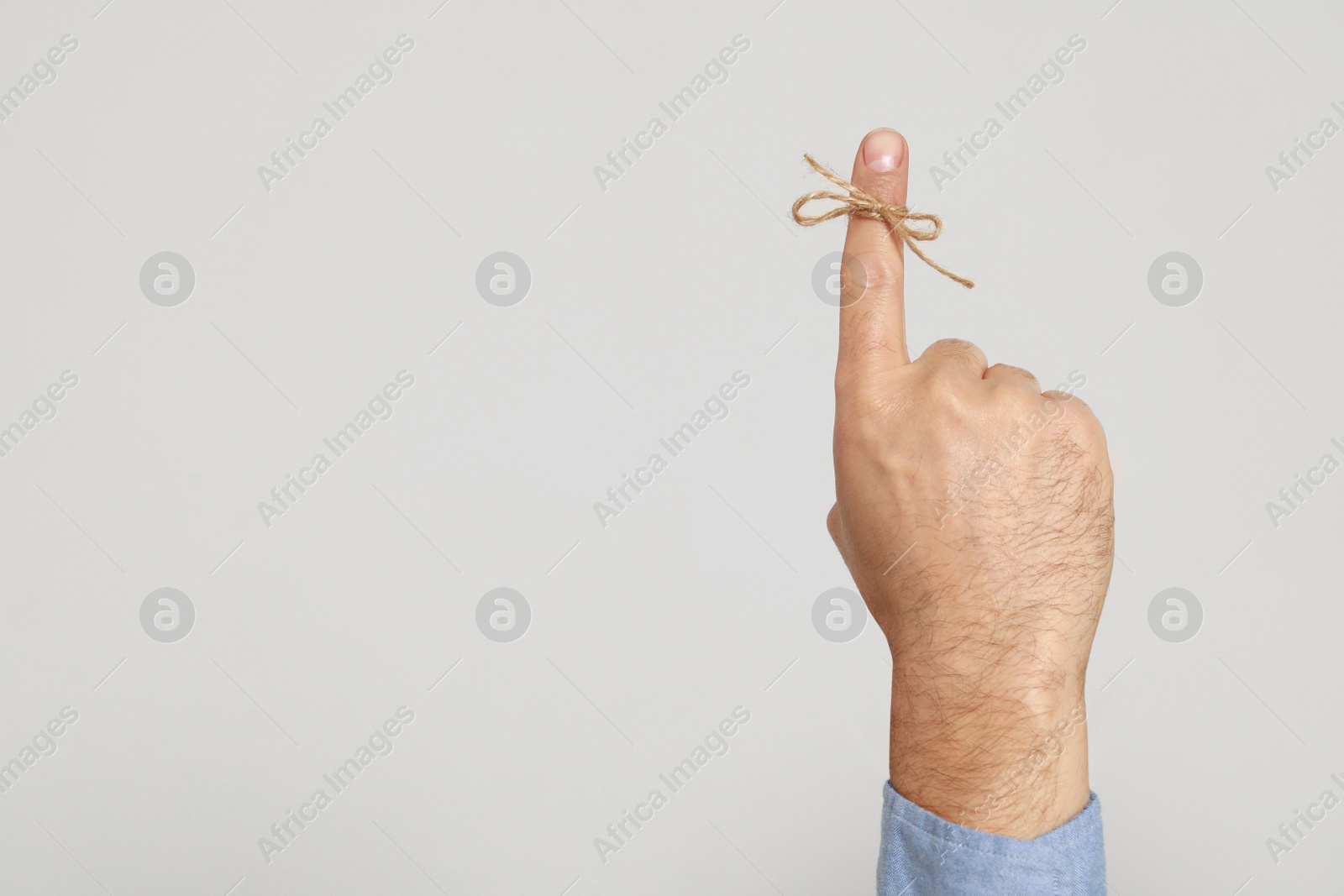 Photo of Man showing index finger with tied bow as reminder on light grey background, closeup. Space for text