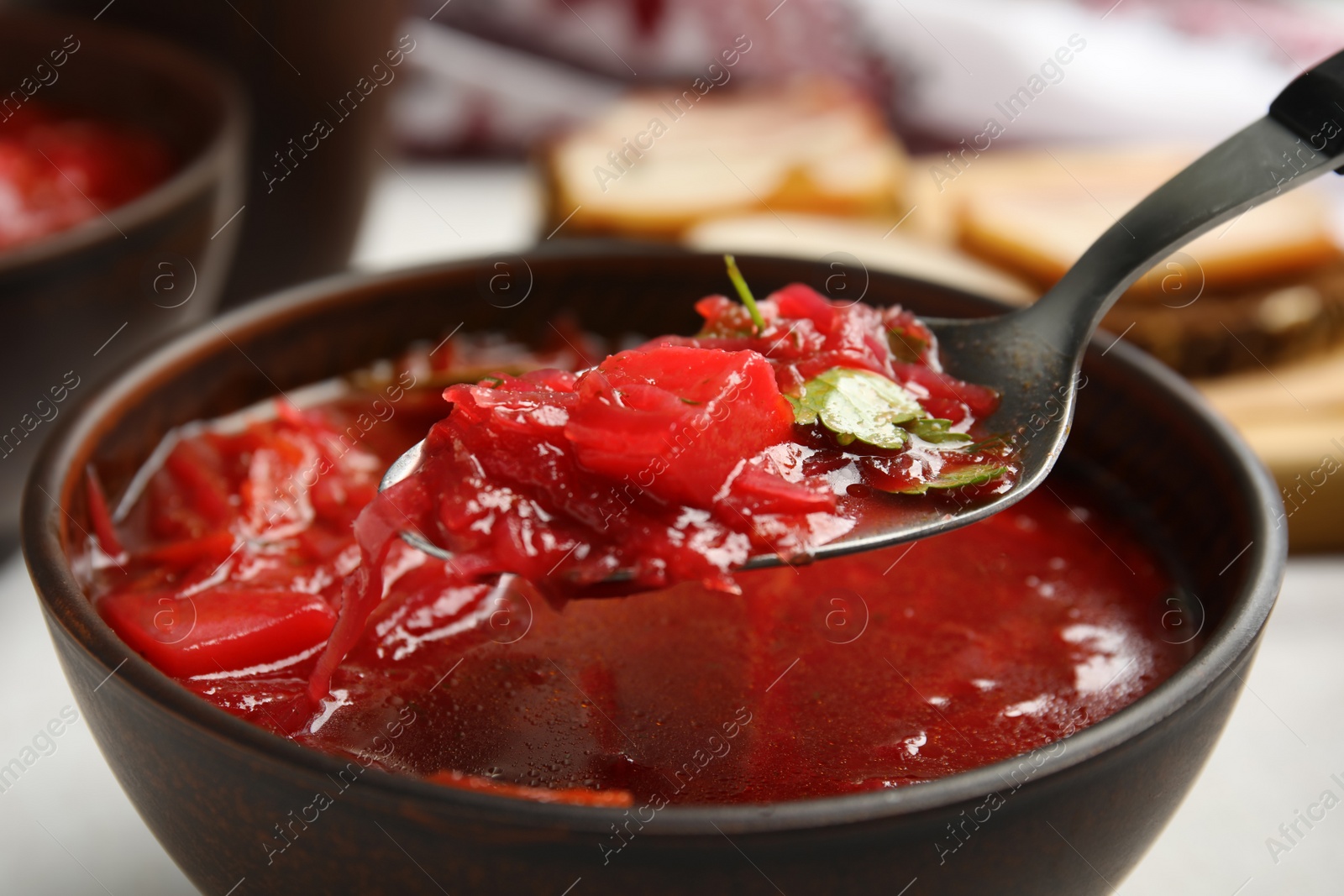 Photo of Spoon with Ukrainian borsch above stylish brown clay bowl, closeup