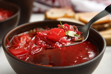 Photo of Spoon with Ukrainian borsch above stylish brown clay bowl, closeup