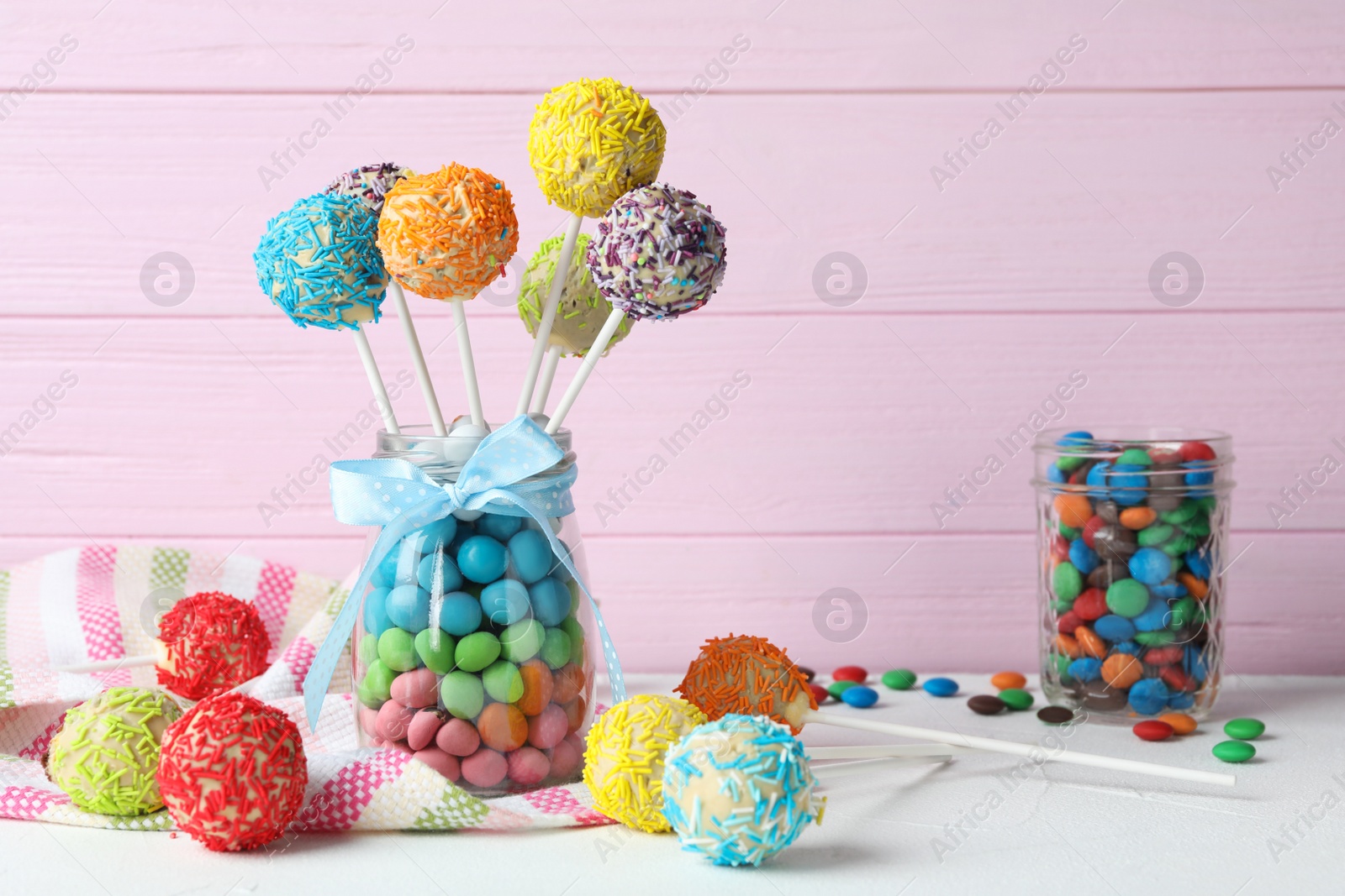 Photo of Yummy bright cake pops in glass jar full of candies on table. Space for text