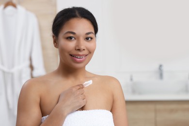 Photo of Young woman applying cream onto body in bathroom. Space for text