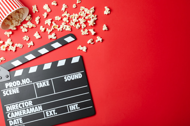 Photo of Clapper board and popcorn on red background, flat lay with space for text. Visiting cinema