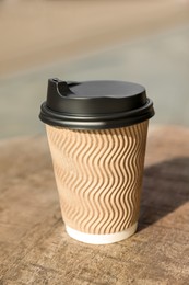 Cardboard takeaway coffee cup with plastic lid on wooden table in city