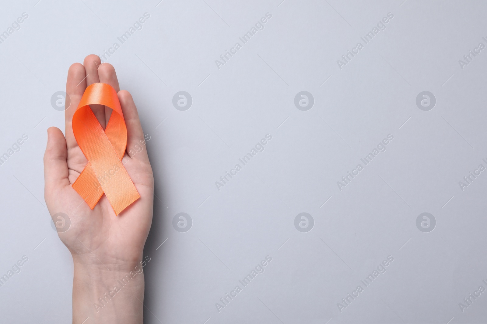 Photo of Man holding orange ribbon on light grey background, top view with space for text. Multiple sclerosis awareness