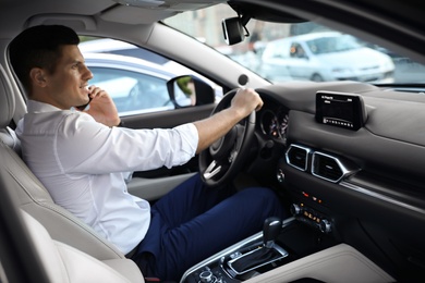 Photo of Handsome man talking on phone while driving his modern car