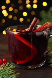 Photo of Aromatic mulled wine and fir branches on wooden table, closeup