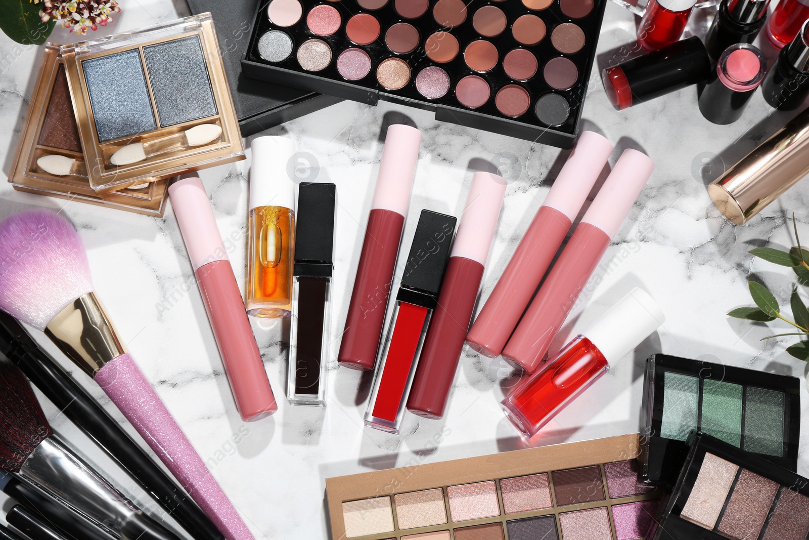 Photo of Bright lip glosses among different cosmetic products on white dressing table