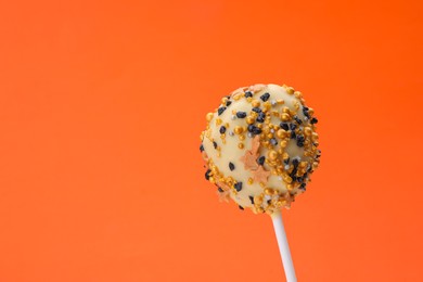 Delicious confectionery. Sweet cake pop decorated with sprinkles on orange background, closeup. Space for text