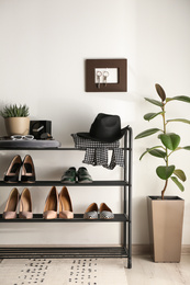 Black shelving unit with shoes and different accessories near white wall in hall