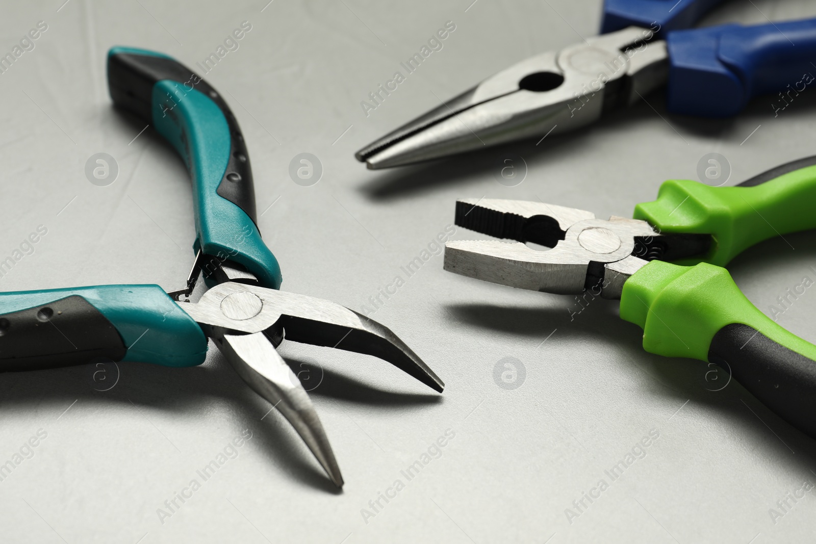 Photo of Different pliers on grey textured table, closeup