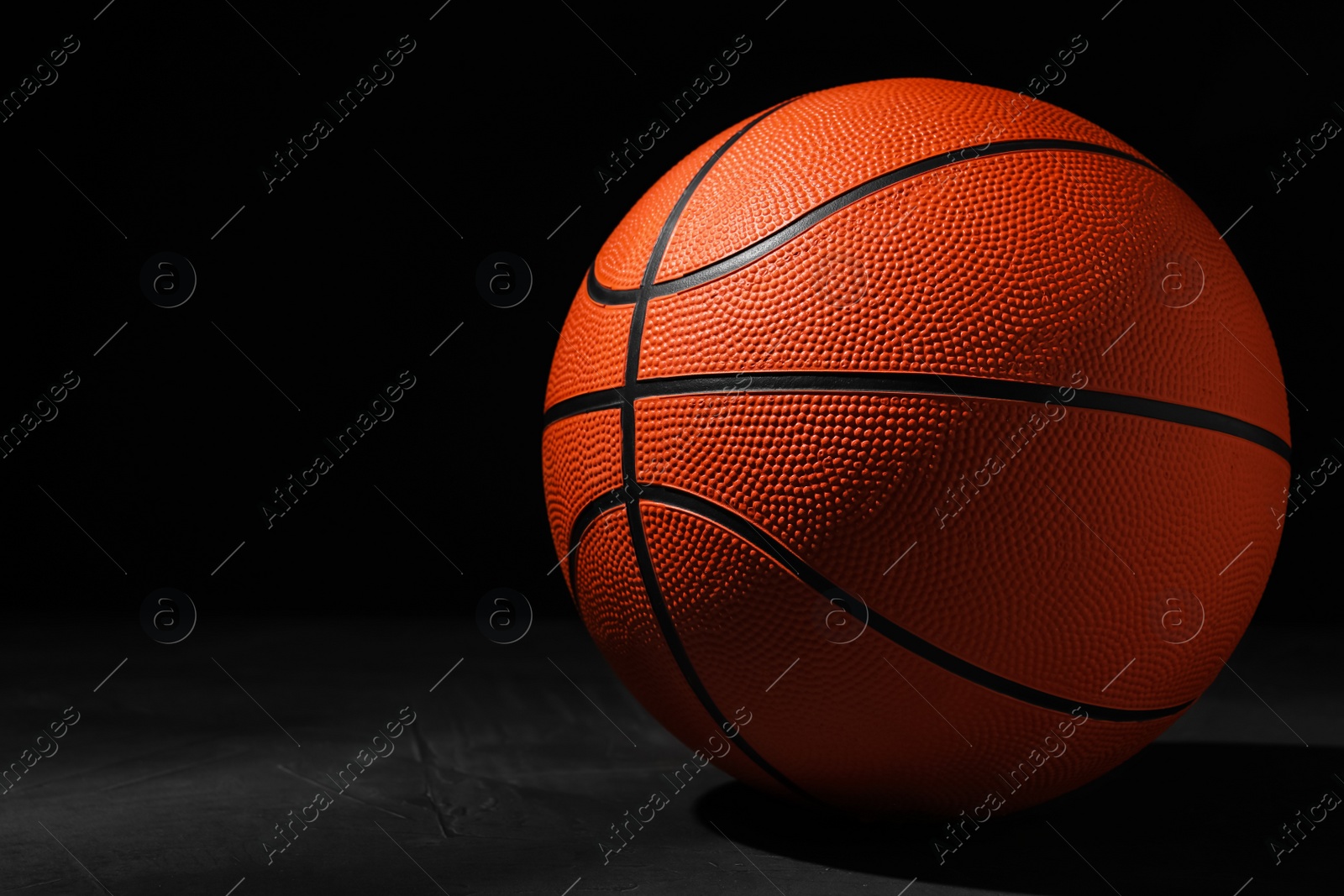 Photo of Basketball ball on grey stone table against dark background, space for text