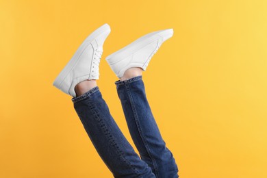 Photo of Man wearing stylish white sneakers on yellow background, closeup