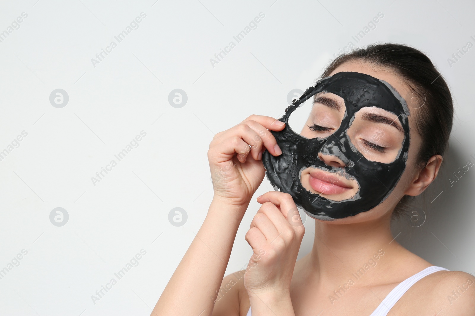 Photo of Beautiful young woman removing black mask from her face on white background. Space for text