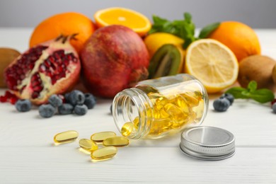 Photo of Vitamin pills, bottle and fresh fruits on white wooden table