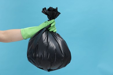 Photo of Woman holding plastic bag full of garbage on light blue background, closeup. Space for text