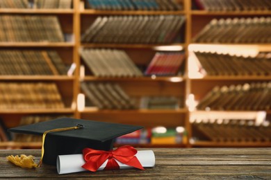 Image of Graduation hat and diploma on wooden table in library, space for text