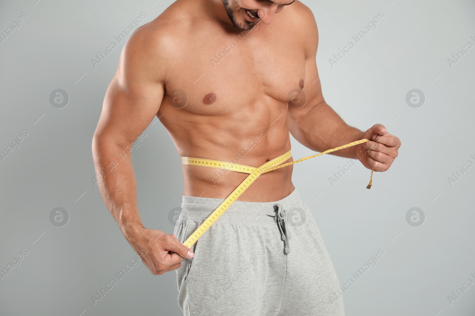 Photo of Young man with slim body using measuring tape on grey background, closeup view