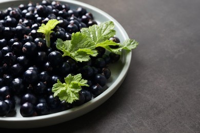 Photo of Plate with ripe blackcurrants and leaves on grey background, closeup. Space for text