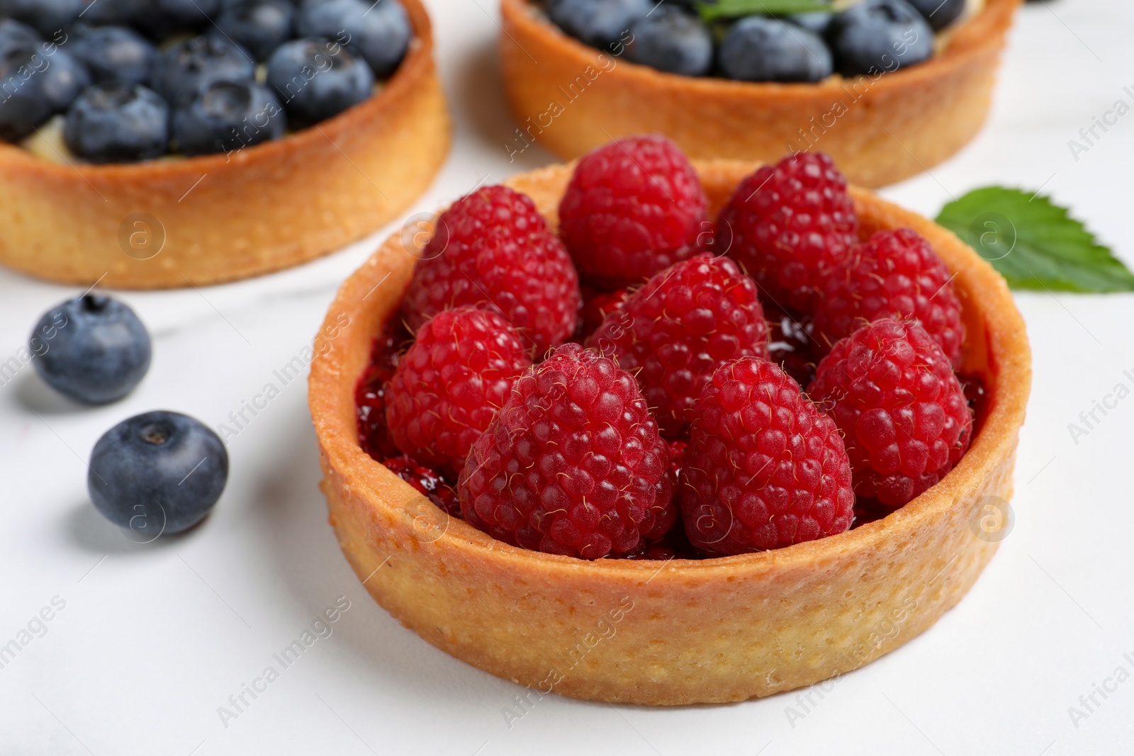 Photo of Tartlet with fresh raspberries on white table, closeup. Delicious dessert