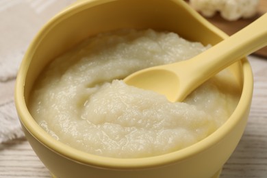 Baby food. Bowl with tasty cauliflower puree on light wooden table, closeup