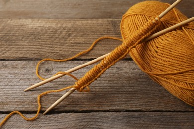 Photo of Soft orange yarn, knitting and needles on wooden table, closeup