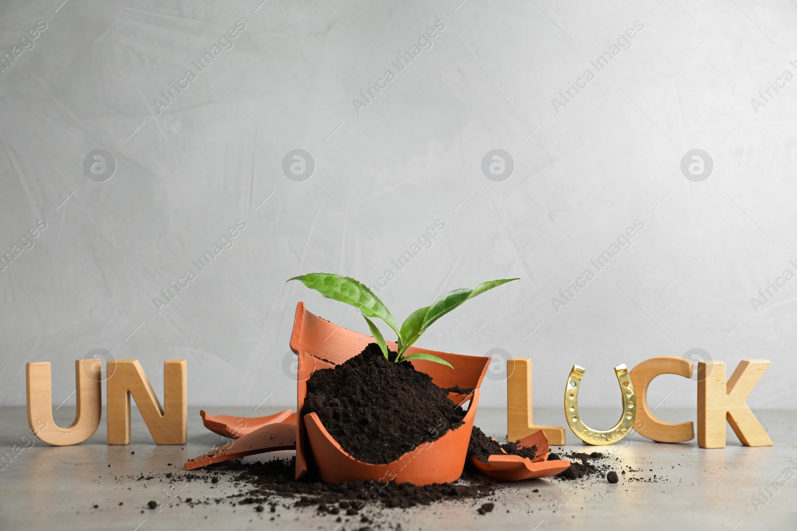 Photo of Word UNLUCK made of wooden letters and plant in broken pot on grey stone table