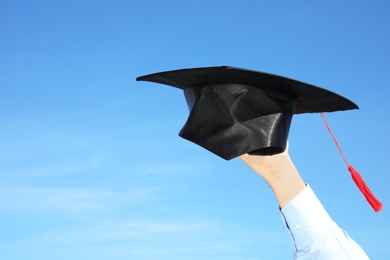 Student with graduation hat and blue sky on background, closeup. Space for text