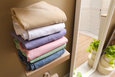 Wooden shelf with stacked clothes on beige wall near mirror. Dressing room interior