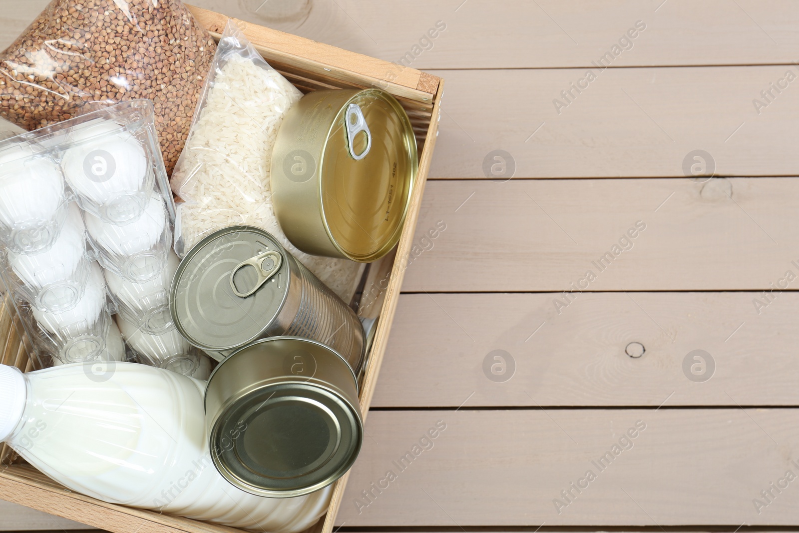 Photo of Donation box with food products on wooden table, top view. Space for text