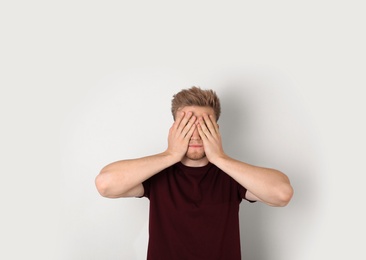 Photo of Young man being blinded and covering eyes with hands on light background