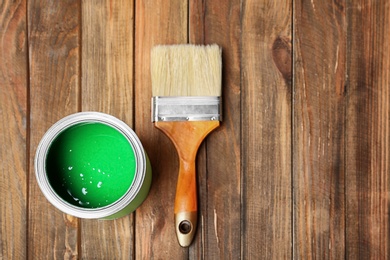 Photo of Tin can with paint and brush on wooden background, top view