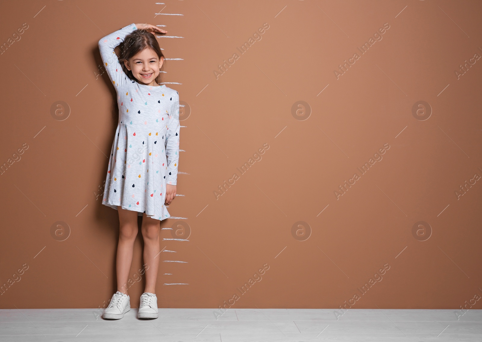 Photo of Little girl measuring her height near color wall