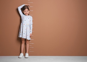 Photo of Little girl measuring her height near color wall