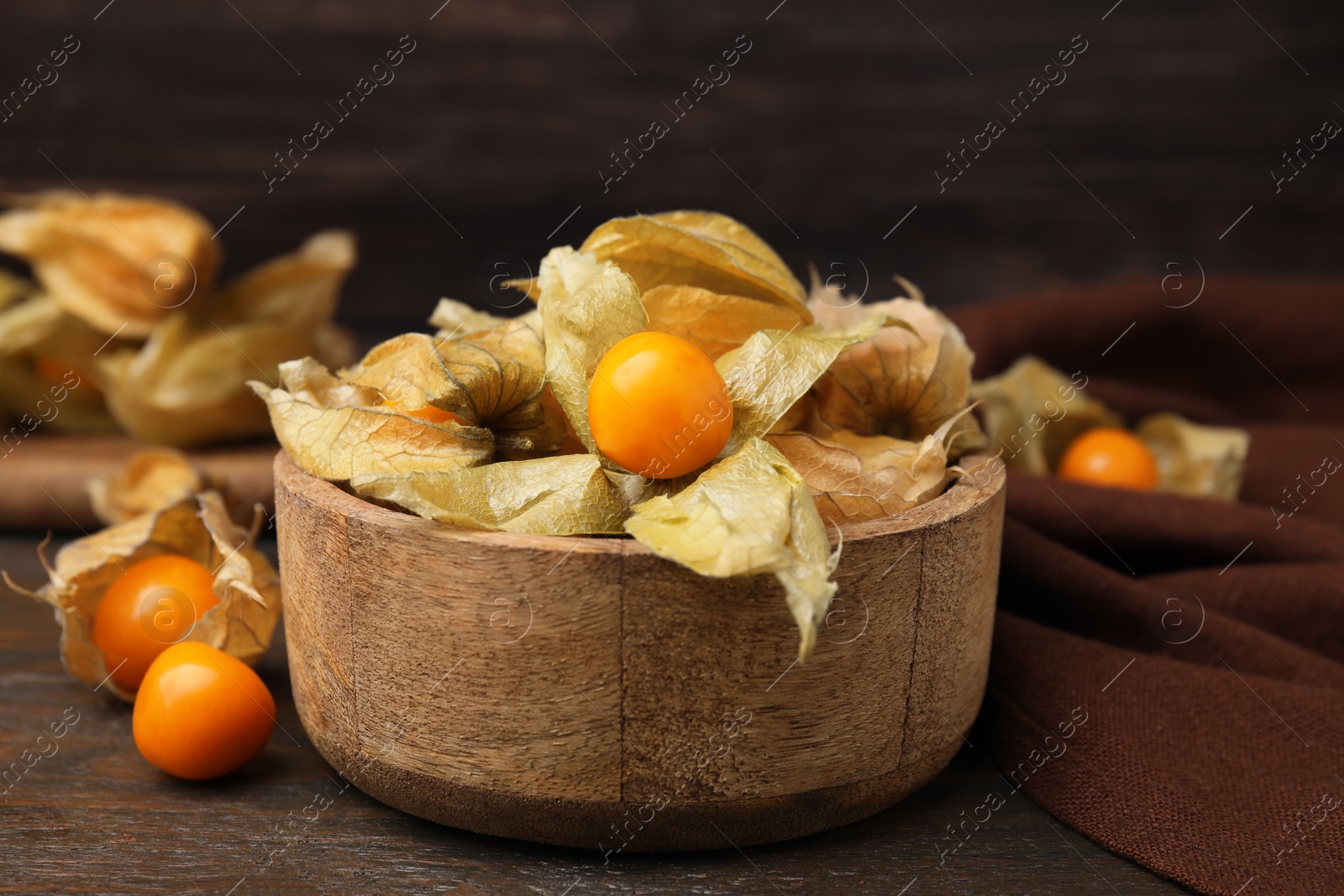 Photo of Ripe physalis fruits with calyxes in bowl on wooden table