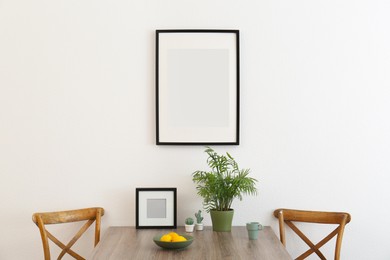 Room interior with dining table, wooden chairs and photo frames on white wall