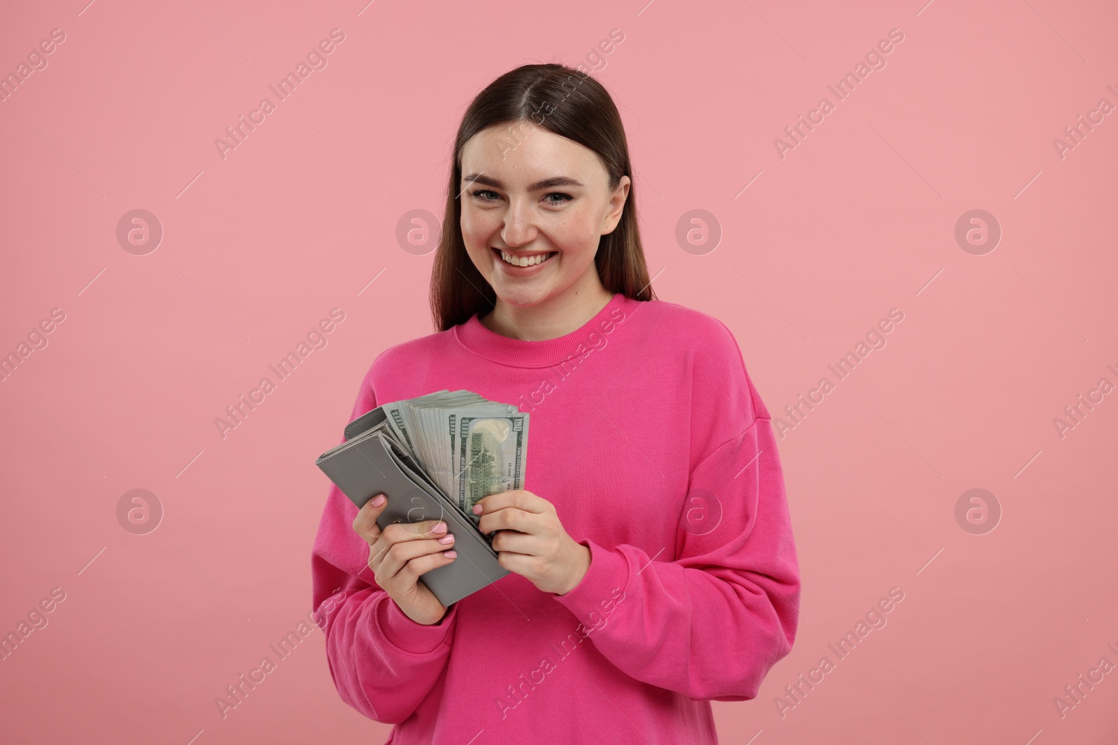 Photo of Happy woman putting money into wallet on pink background