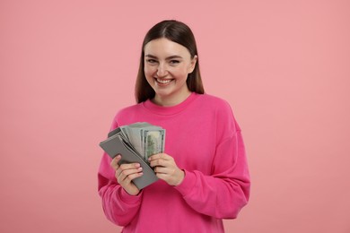 Happy woman putting money into wallet on pink background