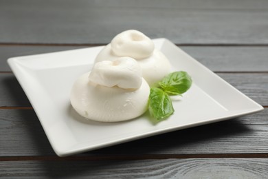Photo of Delicious burrata cheese with basil on grey wooden table