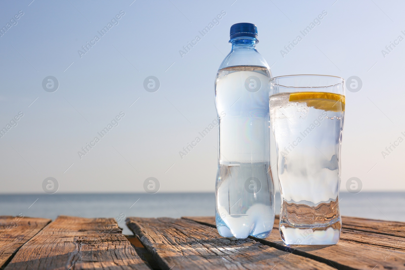 Photo of Wooden table with glass and bottle of refreshing drink on hot summer day outdoors, space for text