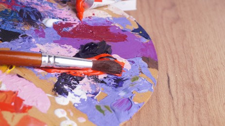 Photo of Artist's palette with mixed paints and brush on wooden table, closeup