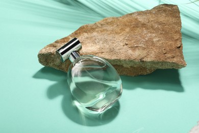 Photo of Bottle of luxury perfume in sunlight and stone on turquoise background