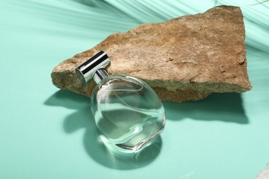 Bottle of luxury perfume in sunlight and stone on turquoise background