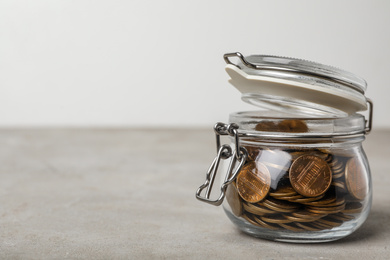 Glass jar with coins on grey table, space for text