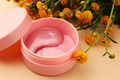 Photo of Jar of under eye patches and beautiful flowers on beige background, closeup. Cosmetic product