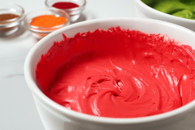 Photo of Bowl of cream with red food coloring on white table, closeup