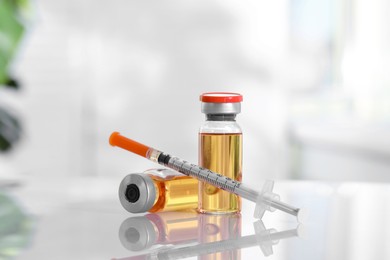 Photo of Glass vials and syringe with orange medication on white table