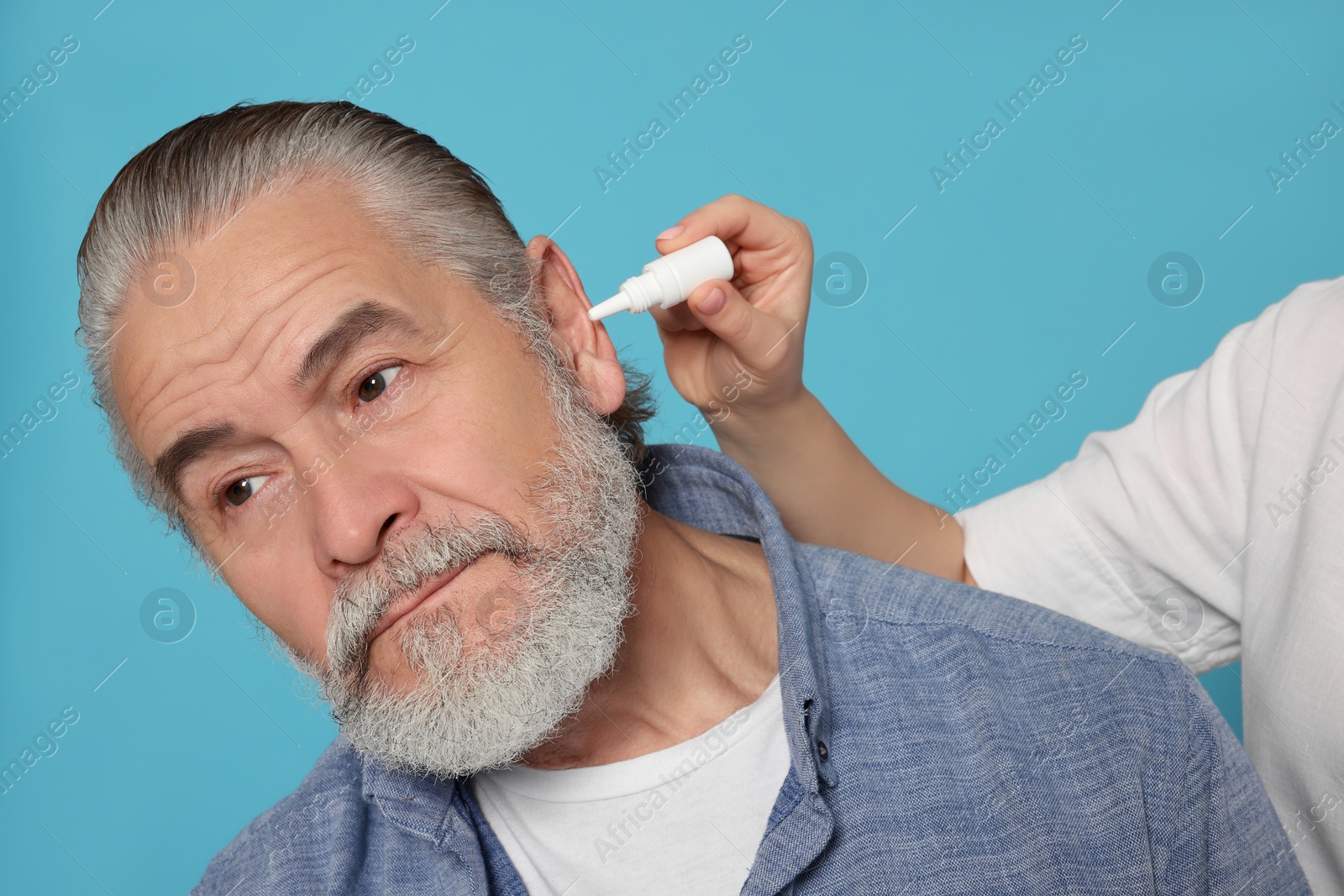 Photo of Young woman dripping medication into man's ear on light blue background