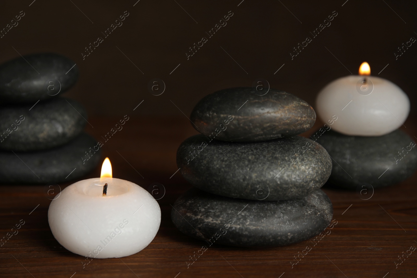 Photo of Burning candles and spa stones on wooden table