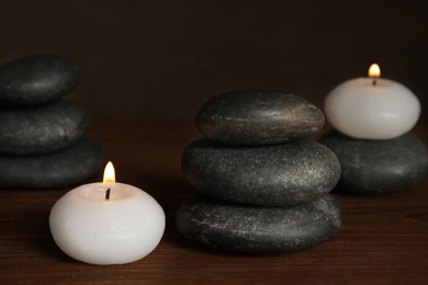 Photo of Burning candles and spa stones on wooden table